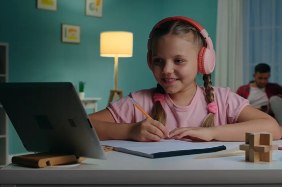 Una niña con sus auriculares mira una pantalla mientras escribe en una libreta