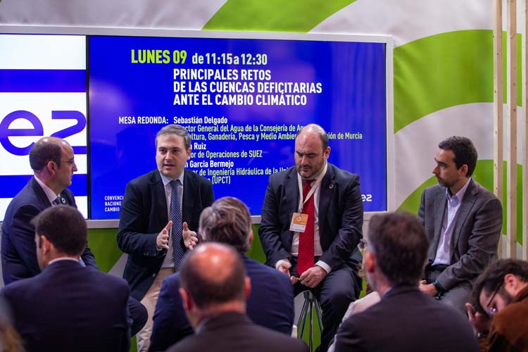 Cuatro personas sentadas ante un panel de presentación se dirigen a un numeroso grupo de personas