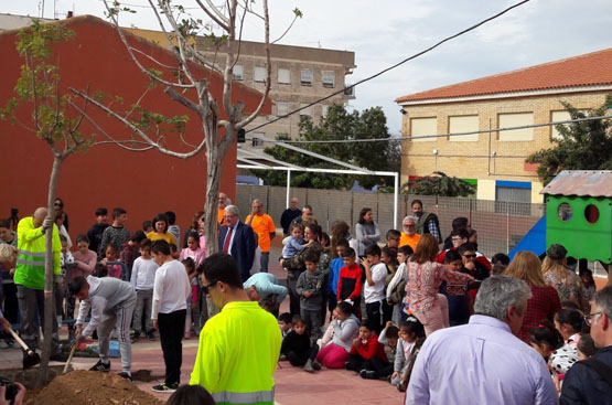 Numerosos escolares acompañados de adultos plantan árboles en el patio de un colegio 